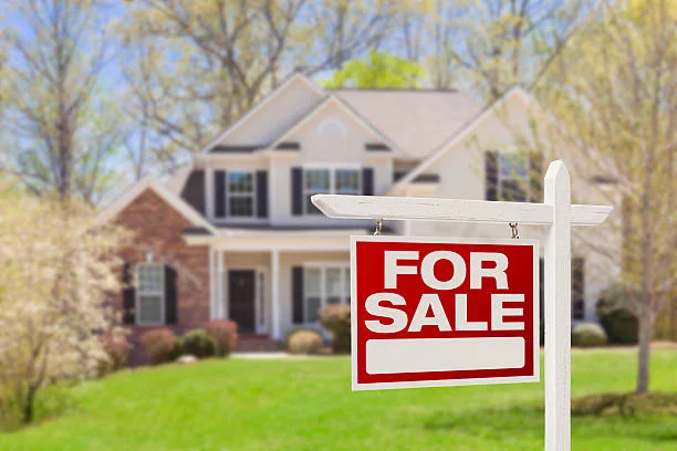 For Sale sign in front of a two-story house in spring