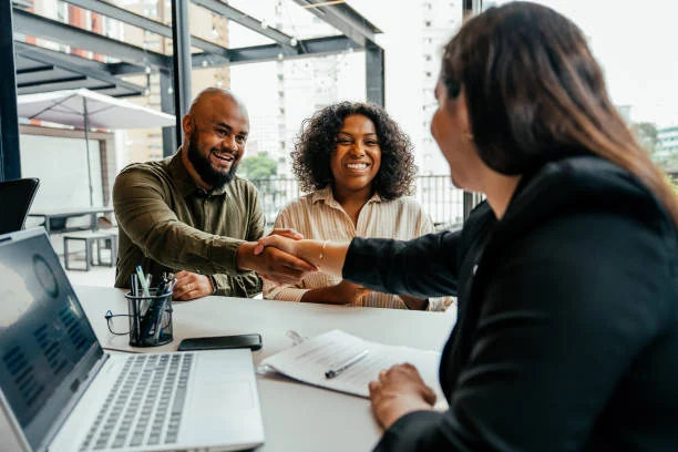 Real estate agent shaking hands with a smiling couple at a desk